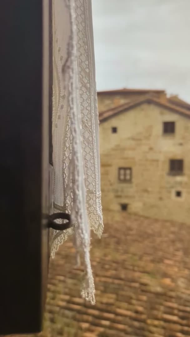 Ventana con visillo de encaje sobre los tejados de Santillana del Mar